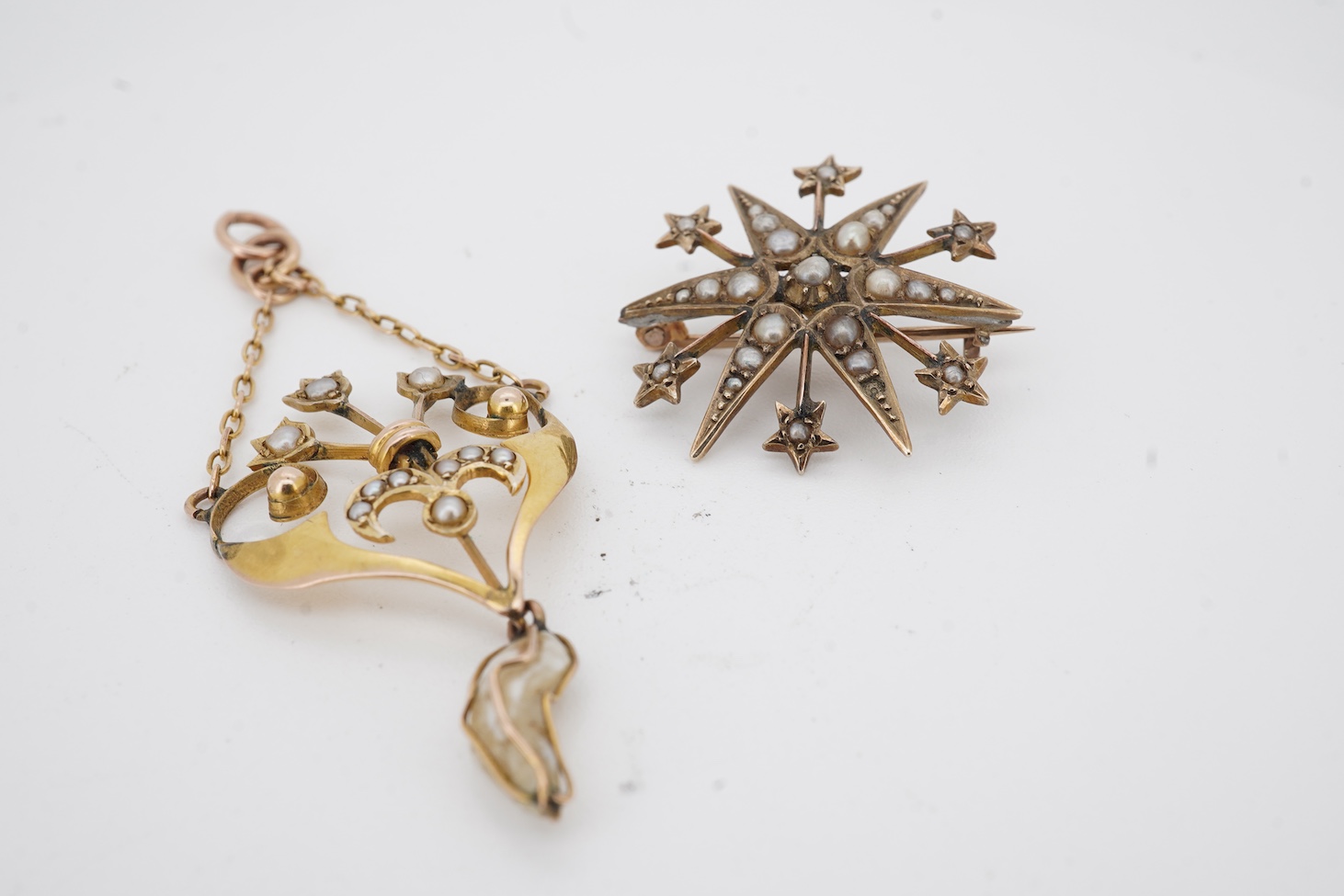 An Edwardian Art Nouveau 9ct, seed and baroque pearl set drop pendant, overall 55mm, together with an Edwardian style 9ct gold and seed pearl set starburst brooch.